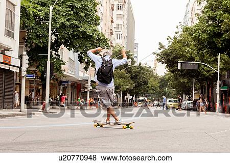 Stock Photo - "Rear view of mature man skateboarding on road, Copacabana town, Rio De Janeiro, Brazil". Fotosearch