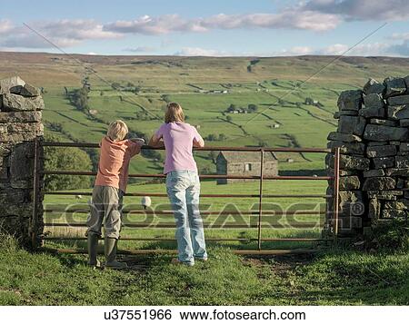 Rear view of teenage girl and brother looking out at farm from gate View Large Photo Image Stock Photograph - Rear view of teenage girl and brother looking out at farm from gate. Fotosearch