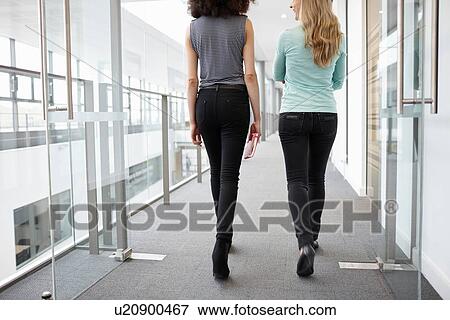 Stock Photo - Rear view of two businesswomen walking along office corridor. Fotosearch