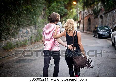 Rear view of young couple strolling on suburban street View Large Photo Image Stock Image - Rear view of young couple strolling on suburban street. Fotosearch