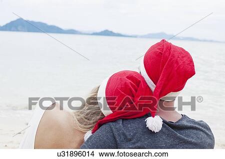 Picture - "Rear view of young couple wearing santa hats on beach, Kradan, Thailand". Fotosearch
