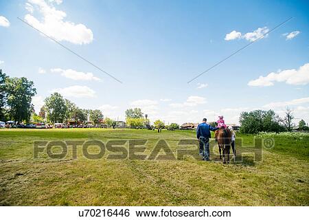 Stock Photograph - Rear view of young man and two girls riding horse in field, Rezh, Sverdlovsk Oblast, Russia. Fotosearch