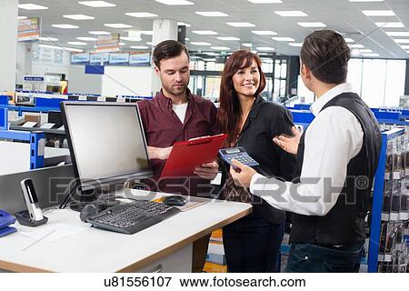 Stock Photo - Sales assistant advising couple on cost in electronics store. Fotosearch