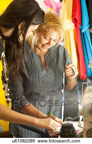 Stock Photo - Seamstress writing clients measurements in sewing shop. Fotosearch