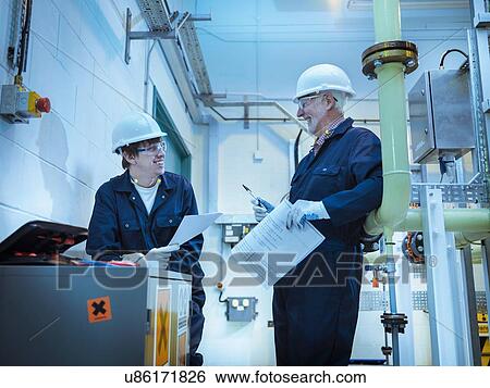 Stock Photograph - Senior and apprentice engineers talking in power station. Fotosearch