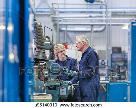 Stock Image - Senior engineer instructing apprentice on factory machinery. Fotosearch
