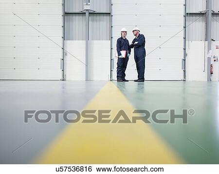 Stock Photograph - Senior engineer instructing apprentice in factory. Fotosearch