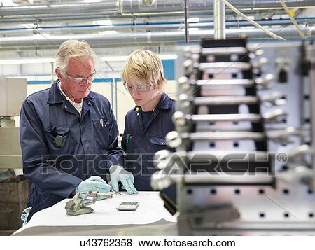 Stock Photo - Senior engineer making calculations with apprentice in factory. Fotosearch