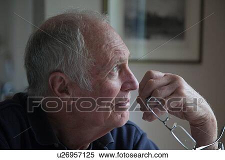 Stock Photography - "Senior man, holding eyeglasses, looking out of window". Fotosearch