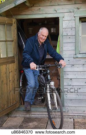 Stock Image - Senior man on bike by shed. Fotosearch