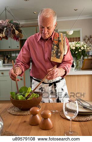 Stock Photo - Senior man preparing salad in kitchen. Fotosearch