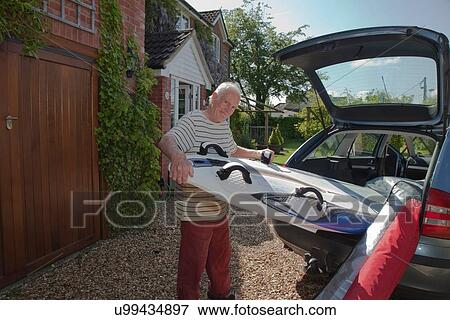 Stock Photo - Senior man removing surfboard from car boot. Fotosearch
