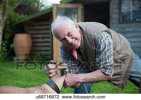 Stock Image - "Senior man, stroking pet dog in garden". Fotosearch