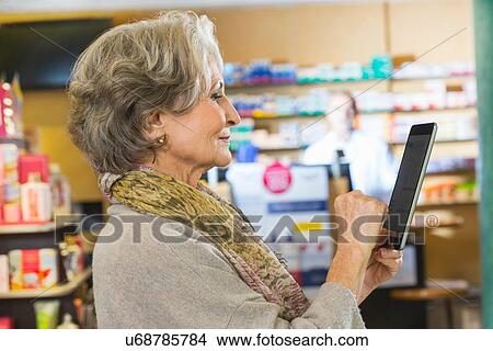 Senior woman using digital tablet to check medicine online in pharmacy View Large Photo Image Picture - Senior woman using digital tablet to check medicine online in pharmacy. Fotosearch