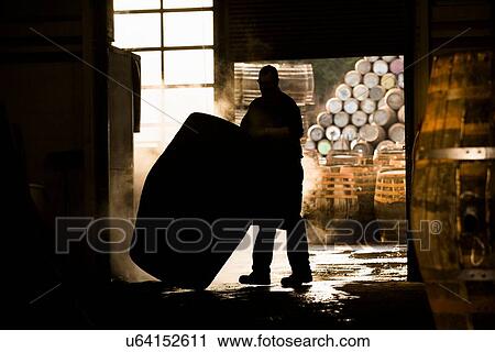 Stock Image - Silhouette of man working in cooperage with whisky cask. Fotosearch