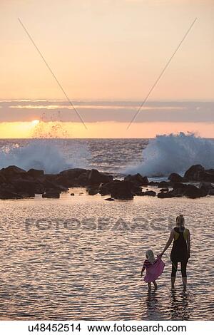 "Silhouetted female toddler and mother paddling in sea looking out at waves splashing, Kona, Hawaii, USA" View Large Photo Image Picture - "Silhouetted female toddler and mother paddling in sea looking out at waves splashing, Kona, Hawaii, USA". Fotosearch