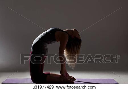 Stock Photo - Silhouetted low key shot of young woman practicing yoga on mat. Fotosearch