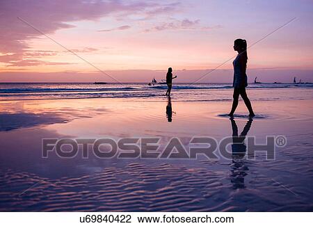 Stock Image - "Silhouetted young woman strolling on beach at sunset, Boracay Island, Visayas, Philippines". Fotosearch