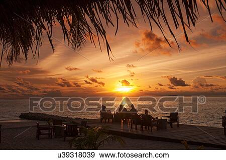 Stock Photo - "Silhouettes of people under palm trees at sunset, Ari Atoll, Maldives". Fotosearch