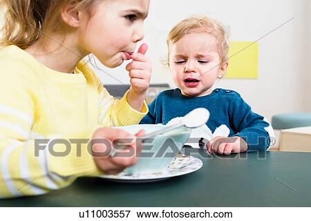 Stock Photo - Sister testing temperature before feeding baby brother. Fotosearch