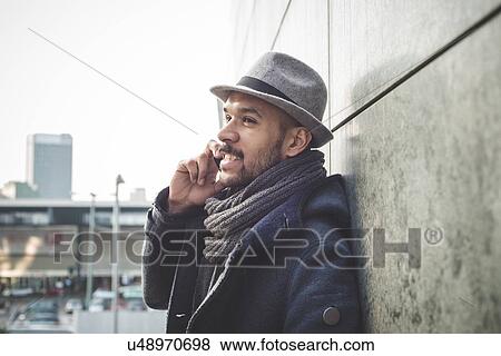 Smiling businessman leaning against wall talking on smartphone View Large Photo Image Stock Photo - Smiling businessman leaning against wall talking on smartphone. Fotosearch