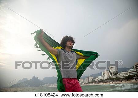 Picture - "Smiling young man holding up Brazilian flag on Ipanema beach, Rio De Janeiro, Brazil". Fotosearch