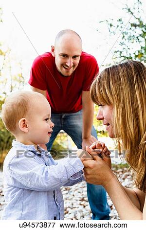 Stock Photo - "Son face to face with mother, holding hands, while father looks on". Fotosearch