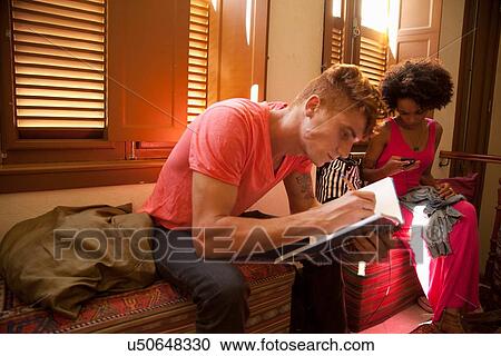 Stock Image - Students chilling out and studying in living room. Fotosearch