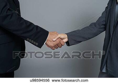 Stock Photograph - Studio close up of young businesswoman and mature businessman shaking hands. Fotosearch