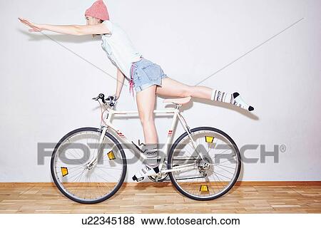 Stock Photo - Studio shot of young woman balancing on one leg on bicycle. Fotosearch