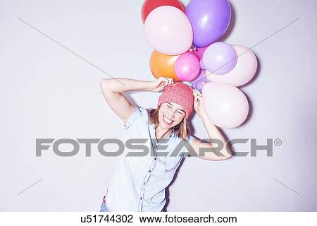 Studio shot of young woman holding bunch of balloons on head View Large Photo Image Stock Image - Studio shot of young woman holding bunch of balloons on head. Fotosearch