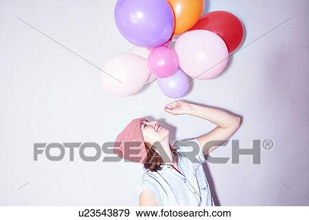 Stock Photo - Studio shot of young woman holding up bunch of balloons. Fotosearch