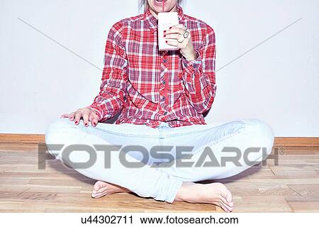 Stock Image - Studio shot of young woman sitting on floor drinking juice. Fotosearch