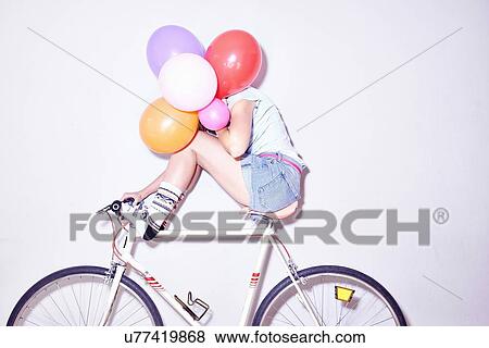Studio shot of young woman sitting on bicycle hiding behind bunch of balloons View Large Photo Image Stock Photo - Studio shot of young woman sitting on bicycle hiding behind bunch of balloons. Fotosearch