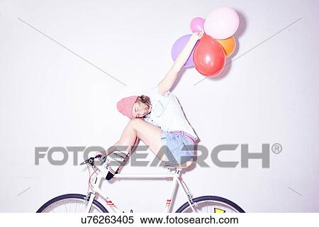 Studio shot of young woman sitting on bicycle holding up bunch of balloons View Large Photo Image Stock Photography - Studio shot of young woman sitting on bicycle holding up bunch of balloons. Fotosearch
