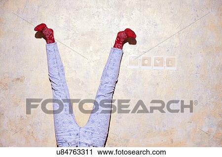 Stock Image - Studio shot of young womans legs upside down against wall. Fotosearch