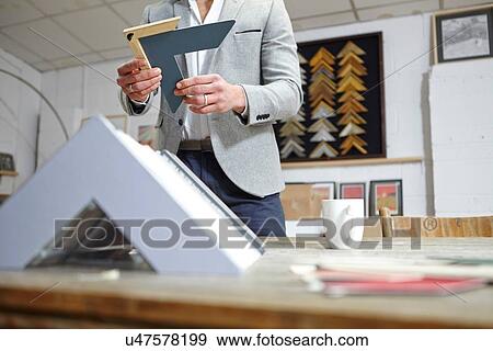 Stock Photo - Surface level view of framer selecting frame in picture framers workshop. Fotosearch