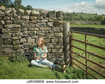 Stock Photo - Teenage girl sitting by dry stone wall in field. Fotosearch