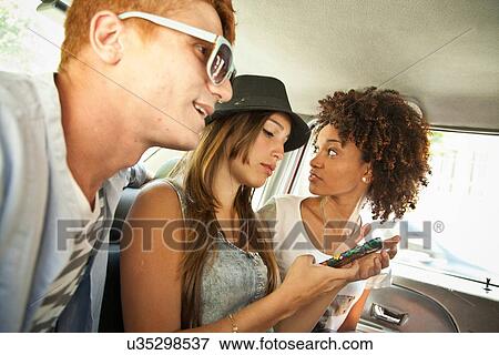 Stock Photo - "Three friends in car, woman using cell phone". Fotosearch
