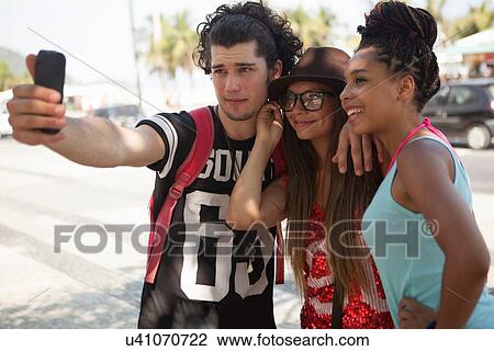 Stock Image - "Three young adult friends taking smartphone selfie, Copacabana, Rio De Janeiro, Brazil". Fotosearch