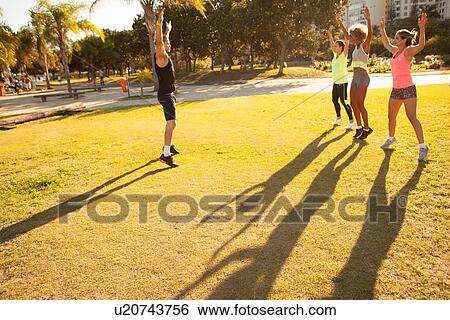 Stock Photograph - Three young women exercising with trainer in park. Fotosearch