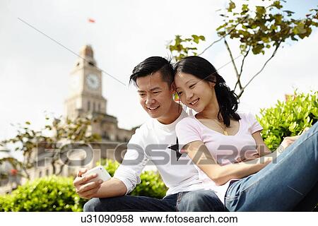 Stock Photo - "Tourist couple looking down at smartphone, The Bund, Shanghai, China". Fotosearch