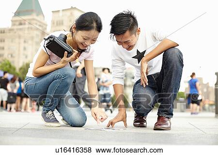 Stock Photo - "Tourist couple looking down on sidewalk at instant film photographs, The Bund, Shanghai, China". Fotosearch