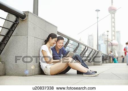 "Tourist couple sitting on bridge looking at digital tablet, The Bund, Shanghai, China" View Large Photo Image Stock Photo - "Tourist couple sitting on bridge looking at digital tablet, The Bund, Shanghai, China". Fotosearch