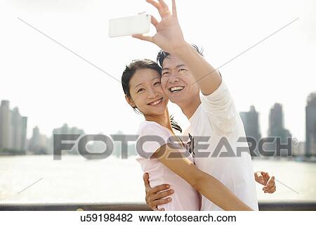 Stock Image - "Tourist couple taking smartphone self portrait, The Bund, Shanghai, China". Fotosearch