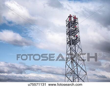 Stock Image - "Tower workers on offshore radio tower on windfarm, low angle view". Fotosearch