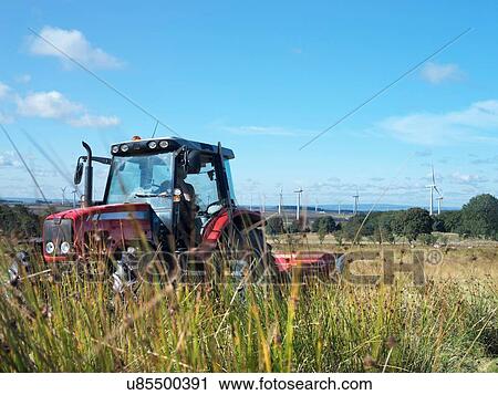 Stock Image - Tractor cutting grass on windfarm. Fotosearch