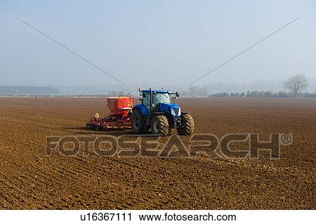 Stock Image - Tractor drilling seed in ploughed field on misty morning. Fotosearch