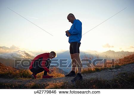 Stock Photograph - "Trail runners resting, one tying shoelace, Valais, Switzerland". Fotosearch