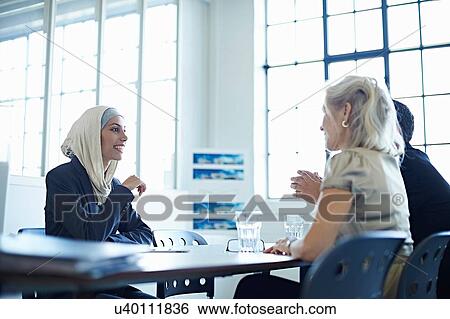 Two businesswomen and man chatting at conference meeting View Large Photo Image Stock Photograph - Two businesswomen and man chatting at conference meeting. Fotosearch